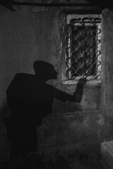 Black and white photo of a Person's shadow is on the wall near window, a burglar who climb into the house through the window. 
