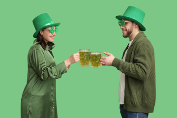 Beautiful young couple in leprechaun hats with glasses of beer on green background. St. Patrick's...