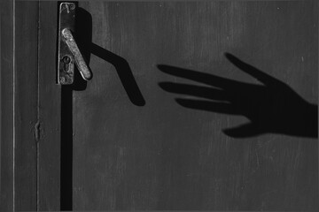 Black and white photo of a shadow of an arm with a hand trying to open a closed door. theft concept. fear. phobia. - obrazy, fototapety, plakaty