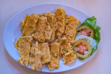 Fried tempeh or tempe goreng, a traditional Indonesian food made from fermented soybean. Served with vegetables on a white plate. 