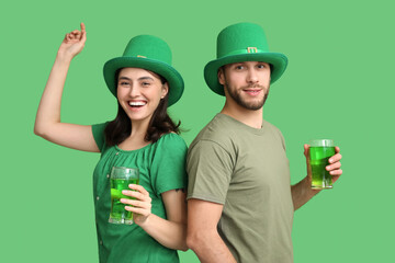 Happy young couple in leprechaun hats with glasses of beer on green background. St. Patrick's Day...