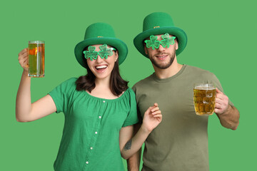 Happy young couple in leprechaun hats with glasses of beer on green background. St. Patrick's Day...