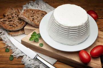 Ricotta cheese with bread, tomatoes and fresh oregano on wooden table.