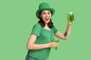 Happy young woman in leprechaun hat with glasses of beer on green background. St. Patrick's Day...