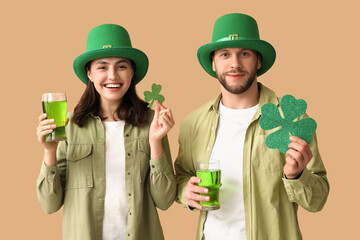 Beautiful young couple in leprechaun hats with glasses of beer and clover on brown background. St....