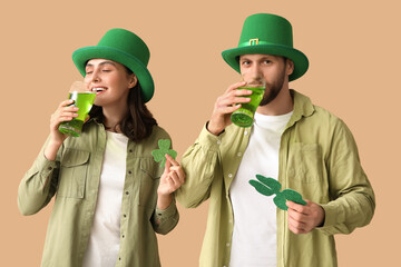 Beautiful young couple in leprechaun hats with glasses of beer and clover on brown background. St....