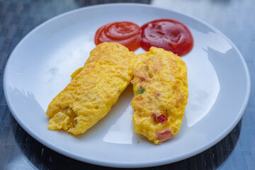 Classic omelet served on a white plate with tomato and hot sauce.