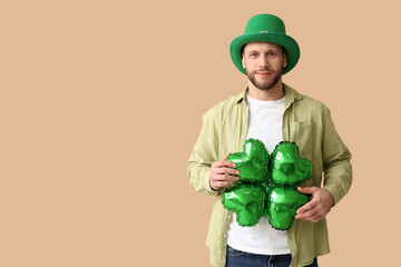 Young man in leprechaun hat with air balloon in shape of clover on brown background. St. Patrick's...