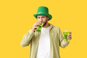 Young man in leprechaun hat with glasses of beer on yellow background. St. Patrick's Day celebration