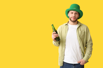 Young man in leprechaun hat with bottle of beer on yellow background. St. Patrick's Day celebration