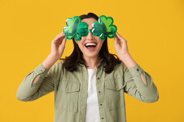 Beautiful young woman with decorative glasses in shape of clover on yellow background. St....