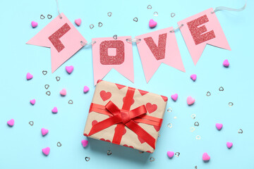 Garland made of paper flags with word LOVE and gift box on blue background. Valentine's Day celebration