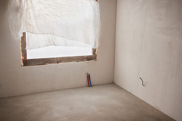 The room is under construction with a rough finish, plastered walls, concrete floor. Wiring of ventilation pipes on a concrete ceiling in a house under construction.