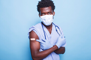 African American nurse with face mask pointing to vaccination injection bandage. After receiving...