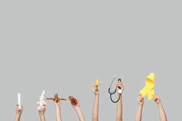Children hands holding toys, stethoscope and yellow ribbons on grey background. International Childhood Cancer Day