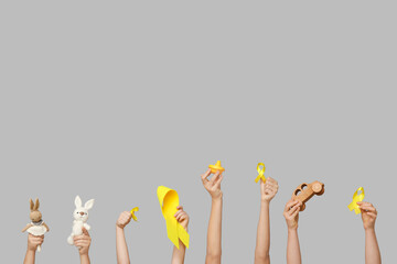 Children hands holding toys and yellow ribbons on grey background. International Childhood Cancer...