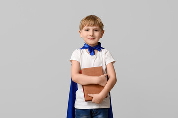 Cute little boy dressed as superhero with books on grey background. Library Lovers Day