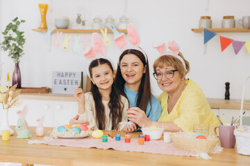 Three generations of women, happy mother with daughter and grandmother painting colorful eggs