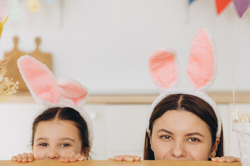 Happy Easter! Young mother and cute daughter wearing bunny ears while hiding behind table