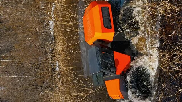 Bright orange marshmobile rides through water and dense reeds, splashing around in a wetland area. Vertical 9x16 Aerial Drone shot