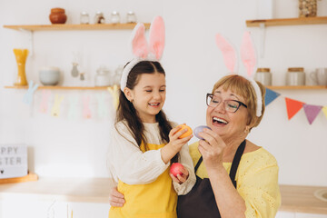 Happy grandmother and granddaughter in easter bunny ears having egg tapping with easter eggs