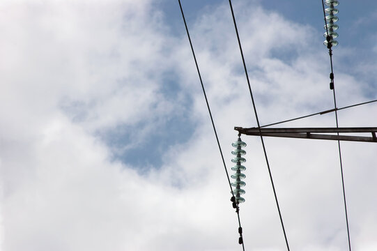 High voltage grid electric power line electricity pilon traverse glass insulators and transmission wires, large detailed steel cables horizontal closeup, bright summer sky cloudscape background