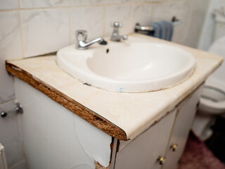 Old worn out cabinet with British style separate tabs for water and sink made of chip wood and in need of repair in small bathroom. Poor quality of living.. Selective focus. Lack of money for repair