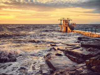 Black rock diving board on Salthill beach in Galway city, Ireland. Warm sunset sky reflects in...