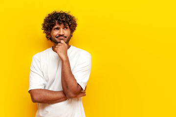 thoughtful curly indian man planning and thinking over yellow isolated background, puzzled guy...