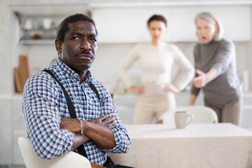 Tense man listens to two women shouting at him in the kitchen