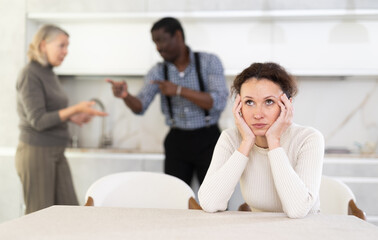 Upset woman tired of domestic quarrel. Husband and mother in law quarreling in the background