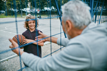 Grandfather watching his grandson play basketball at an outdoor basketball court
