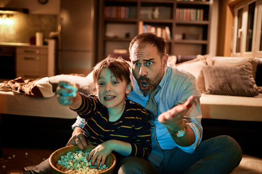 Father and son watching a soccer match and cheering for their favorite team while eating popcorn