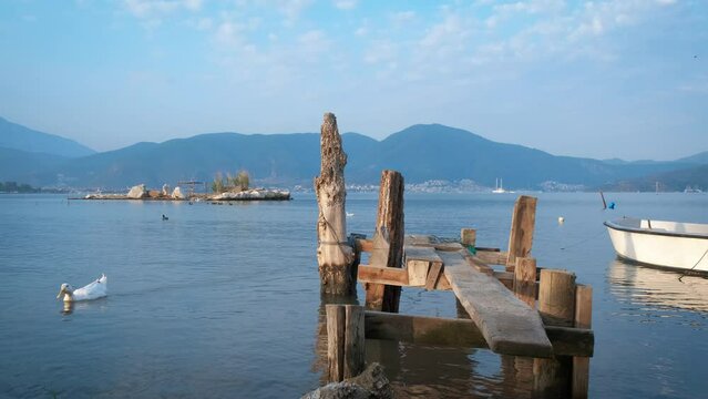 Wooden handmade pier in sun. A view of sunny day with wooden handmade pier and fishing baot in lake water against mountains in summer.