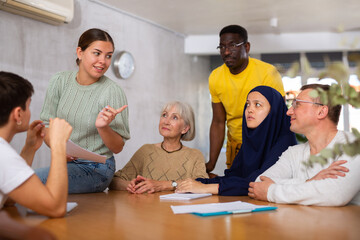 Group of multinational men and women discussing document while sitting at table in office..