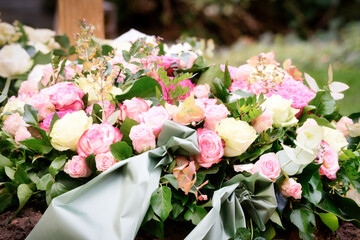 funeral flower wreath of pink and yellow roses and gray-green ribbon on a grave after a funeral