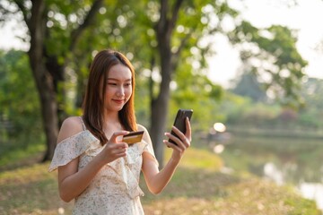 Asian woman holding a credit card and using phone to manage her transaction online via banking app