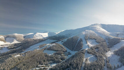 Aerial winter view of Demanovska Dolina village in Low Tatras mountains, Slovakia. Drone panoramic view to ski resort houses among coniferous forest in snow and ice, snowy cable car station at sunset © Flash Vector