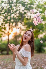 Young Asian beauty enjoys playing and posing with sakura flowers at a public park during sunset moments