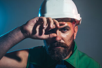 Closeup portrait of tired builder in construction helmet. Fatigued worker wipes sweat from forehead. Hard work at construction site. Heavy profession. Handsome male architect or engineer in hard hat. - obrazy, fototapety, plakaty