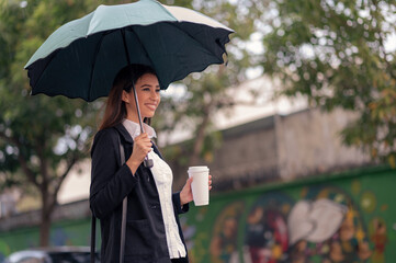 An executive woman in a black jacket walks down the street on a rainy day with an umbrella and...