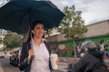 A woman in a black coat under an umbrella crosses a  street in the rain.
