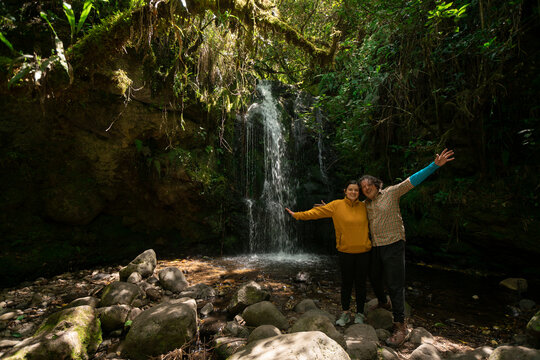 Couple taking photos next to a waterfall in the middle of a forest during a sunny day