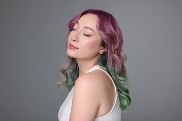 Naklejka premium Trendy hairstyle. Young woman with colorful dyed hair on grey background