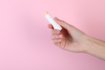 Woman with lip balm on pink background, closeup