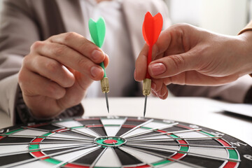 Business targeting concept. Man and woman with darts aiming at dartboard at table, closeup