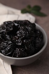 Sweet dried prunes in bowl on brown table, closeup