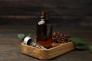 Clove oil in bottle, pipette and dried buds on wooden table, closeup