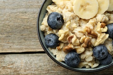 Tasty oatmeal with banana, blueberries and walnuts served in bowl on wooden table, top view. Space for text