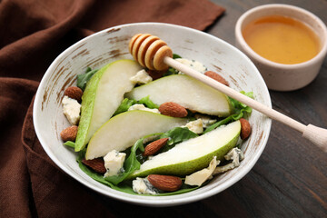 Delicious pear salad in bowl, honey and dipper on wooden table, closeup